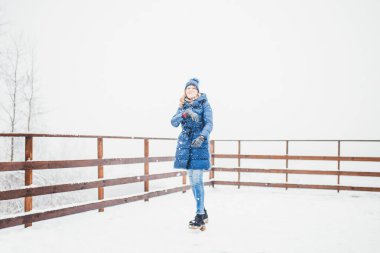 Uzun mavi ceketli, uzun boylu, ince bir sarışın ve kışın örülmüş bir şapka beyaz karda kameraya kartopu atıyor. Kar taneleri uçuşuyor.