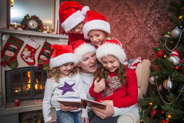 Vader Leest Kerstboek Voor Kinderen Bij Open Haard Onder Kerstboom — Stockfoto