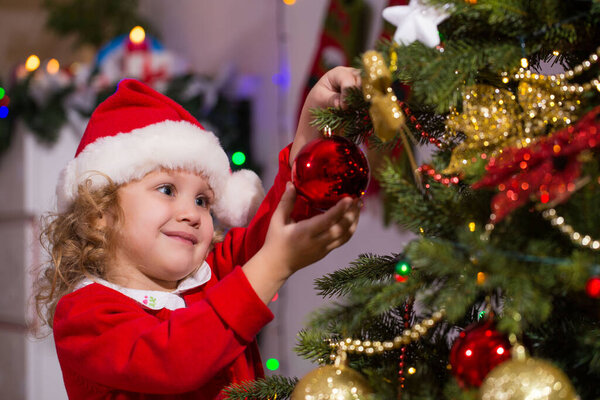 Little girl in Santa hat decorates a Christmas tree