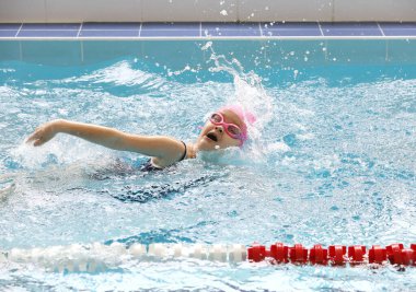 Yüzme eğitiminde havuzda yüzen küçük kız.