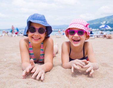 Küçük kızlar kumsalda oynuyorlar ve güneşleniyorlar.