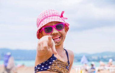 Küçük kız kumlu bir sahilde uzanıyor ve güneşte güneşleniyor.