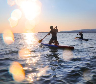 Günbatımında denizde sörf yapan genç insanlar.