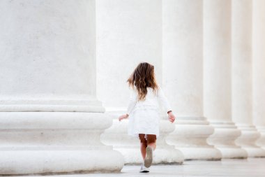 Trieste, İtalya - 10 Ekim 2020 'de sütunların yanında koşan güzel küçük bir kızın arka görüntüsü