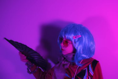 Bir fuşya arka planında fotoğraf çekimi için yelpazeyle poz veren küçük bir kız.