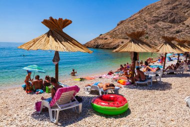 Stara Baska, Hırvatistan - 21 Temmuz 2020 'de güzel Oprna plajında hasır şemsiyeler altında yıkanır