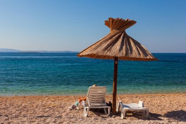 Hırvatistan 'ın Krk adasındaki Oprna plajında saman şemsiyesi altında kitap okurken güverte sandalyesinde dinlenen kız