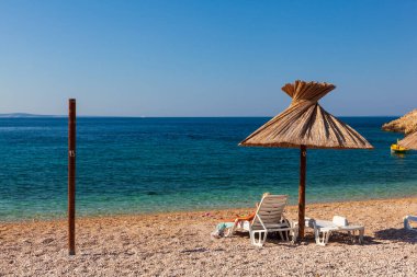 Hırvatistan 'ın Krk adasındaki Oprna plajında saman şemsiyesi altında kitap okurken güverte sandalyesinde dinlenen kız