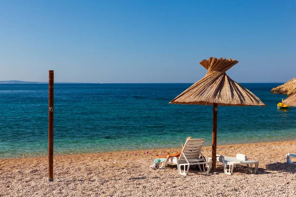 Hırvatistan 'ın Krk adasındaki Oprna plajında saman şemsiyesi altında kitap okurken güverte sandalyesinde dinlenen kız