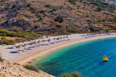 Hırvatistan 'ın Krk adasındaki Oprna plajında saman şemsiyesi altında kitap okurken güverte sandalyesinde dinlenen kız