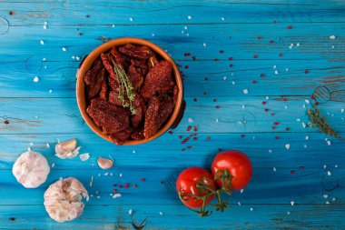 Bir kasenin içindeki Akdeniz kurutulmuş domateslerinin üst görüntüsü, sarımsak ve taze domatesler mavi kırsal ahşap üzerinde