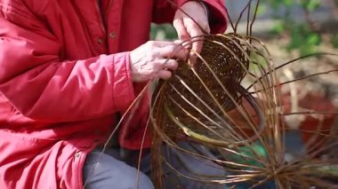 Yaşlı adam caddede hasır sepet örüyor.