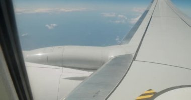 Uçaktan bir görüntü. Uçak bulutların arasında uçuyor. Uçağın kanatları çerçevede görünür.