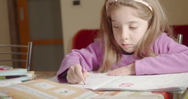 Evde ödevlerini yapan küçük bir kız kahverengi kalemle okul kitabını çiziyor.