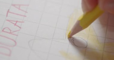 Bir kızın eli, sarı kalemle güneşin resmini boyuyor.