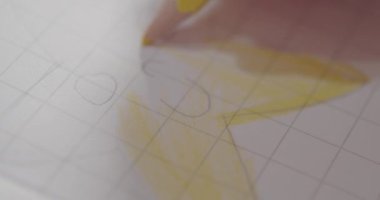 Bir kızın eli, sarı kalemle güneşin resmini boyuyor.