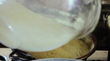 Polenta adında geleneksel bir hominy yemeği olan bakır bir cualdron ile kaynaşıp karıştırmak. Bu, tarihsel olarak diğer tahıllardan yapılmış bir haşlanmış mısır unu tabağıdır. Sıcak yulaf lapası olarak servis edilebilir..