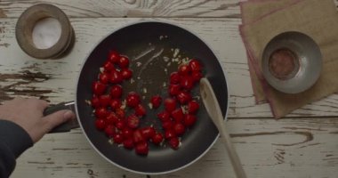 Tavada kızartılmış sarımsaklı domates pişirme manzarası. Aşçı ahşap kepçeyle karışıyor.