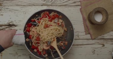 Datterini 'li spagetti, kızarmış sarımsaklı domates ve tavada deniz ürünleri pişirme manzarası. Aşçı ahşap kepçeyle karışıyor.