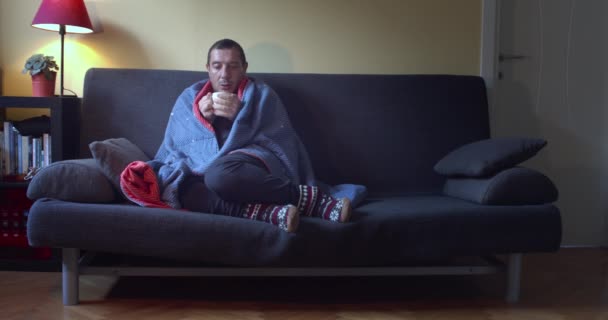 Chory Człowiek Grypą Siedzący Kanapie Owinięty Niebieski Koc Pijąc Gorącą — Wideo stockowe