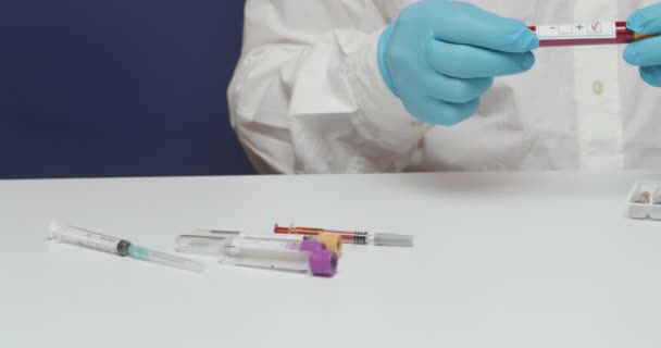 分析实验室的医生手在摄像机前展示了一位病人包扎的血检结果 测试结果写在试管里 医生穿着一件白色的外套和蓝色的手套 — 图库视频影像
