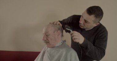 Adam evde saç makasıyla beyaz saçlı bir adamın saçını kesiyor.