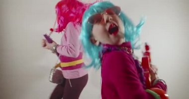 Komik, sevimli, mutlu kız gitarist ve mikrofonda şarkı söyleyen güneş gözlüğü ve renkli peruklar takan müzik eşliğinde dans eden kızlar.