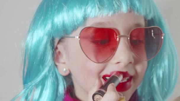 선글라스를 파란색 가발을 스러운 소녀는 입술에 립스틱을칠 앞에서 화장을 배우고 — 비디오