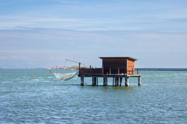 Kırsal ahşap bir stilt ev ve balıkçı ağları ile tekne sakin bir lagünün üzerinde, Pellestrina