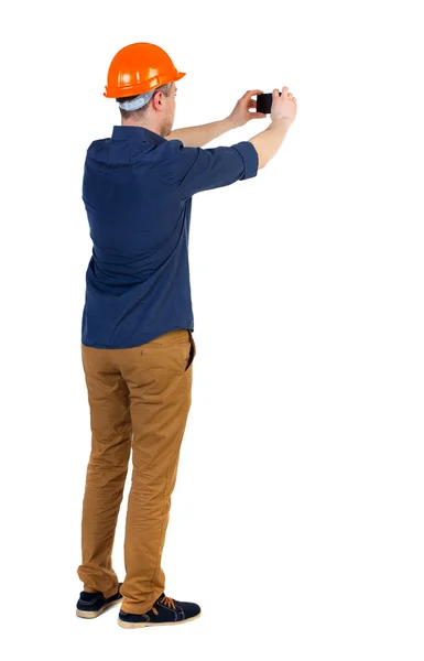 Backview of an engineer in construction helmet stands and using — Stock Photo, Image