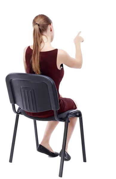 Widok z młoda piękna kobieta siedzi na krześle i pointin z tyłu — Zdjęcie stockowe