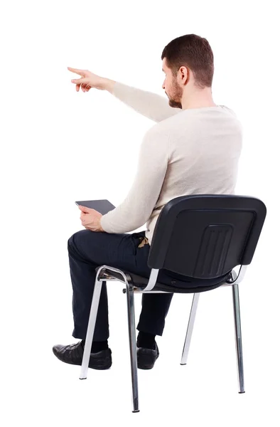 Back view of pointing man sitting on chair and looks at screen o — Photo