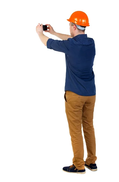 Backview of an engineer in construction helmet stands and using — Stock Photo, Image