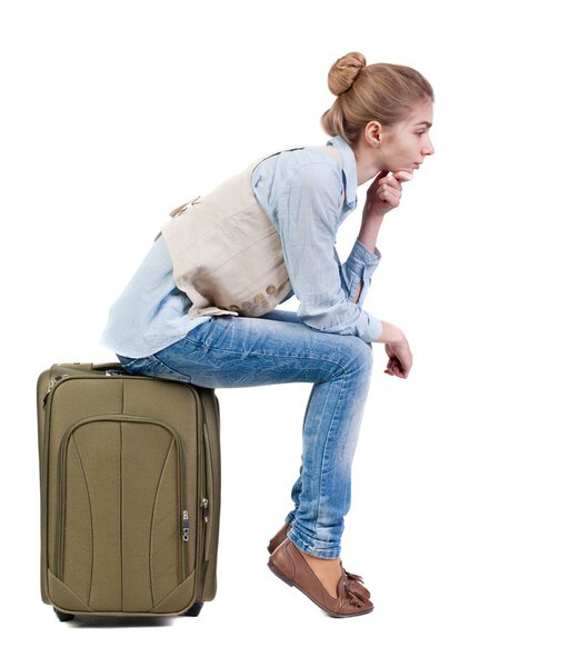 back view of woman  in vest sits on a suitcase.