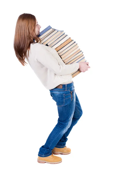 Uma garota carrega uma pilha pesada de livros. — Fotografia de Stock