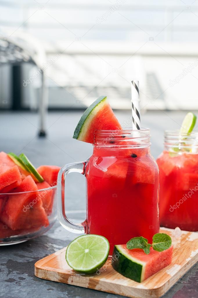 Watermelon juice and slices with lime on black table