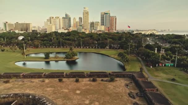 Paisaje del parque diseñado en la orilla del estanque aérea. Rascacielos modernos sobre plantas y árboles tropicales verdes — Vídeo de stock