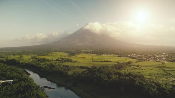 Ο ήλιος λάμπει πάνω από ηφαίστειο Mayon εκρήγνυται εναέρια. Ποτάμι στην καταπράσινη πλαγιά του λόφου. Τροπικό δάσος στο Legazpi — Αρχείο Βίντεο