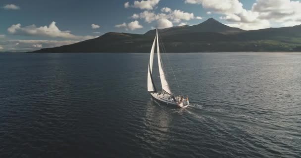 In Zeitlupe segelt die Jacht an der Küste der Berginsel aus der Luft. Weißes Segelboot in Arran, Schottland, Europa — Stockvideo