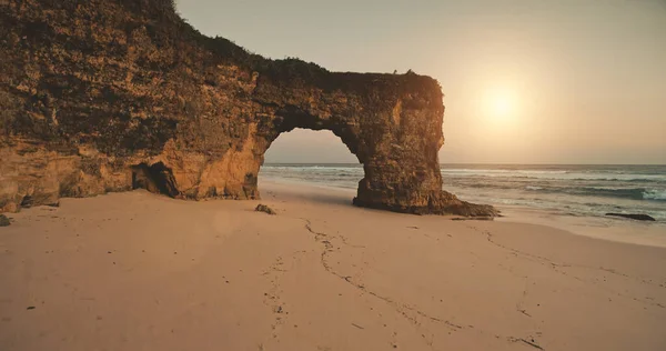 Acantilado única pared con agujero gigante en la luz del sol aeial. Playa de arena en las olas de la bahía del océano. Nadie naturaleza — Foto de Stock