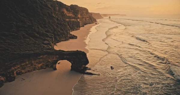 Puesta de sol en la pared de roca en la playa de arena vista aérea. Nadie paisaje de la naturaleza del océano paisaje marino con olas — Foto de Stock