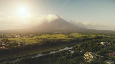 Sun shine over Mayon volcano erupts aerial. River at green grass hillside. Tropic forest at Legazpi clipart