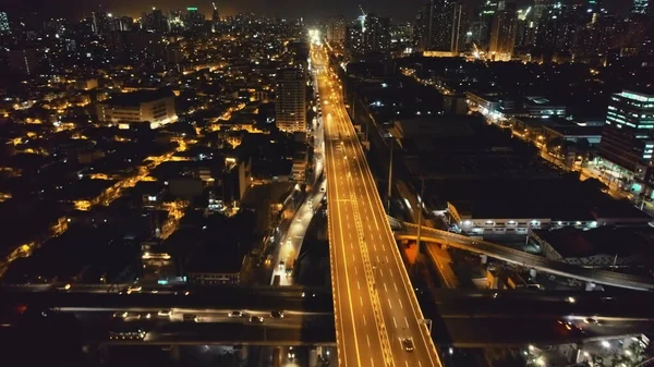 Carretera de tráfico nocturno en cámara lenta a la vista aérea del paisaje urbano crepuscular. Drone volando por encima del paso elevado urbano — Foto de Stock