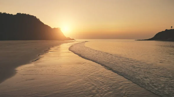 海浪下的夕阳西下,沙滩被冲刷.空中的太阳落在山的轮廓上.热带无人自然 — 图库照片