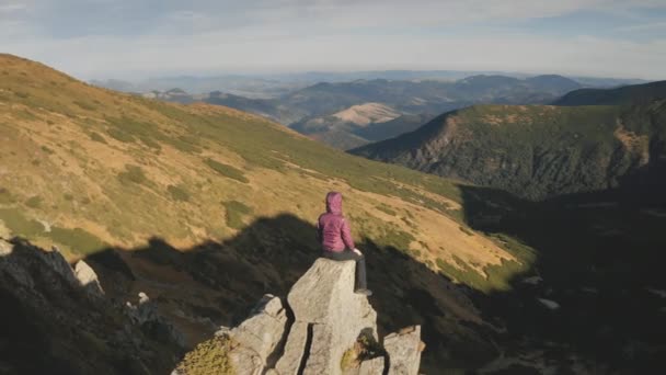 Mujer levantando manos aéreas. Chica turística se sienta en la cima de la roca de montaña. Naturaleza paisaje en el día de otoño — Vídeos de Stock