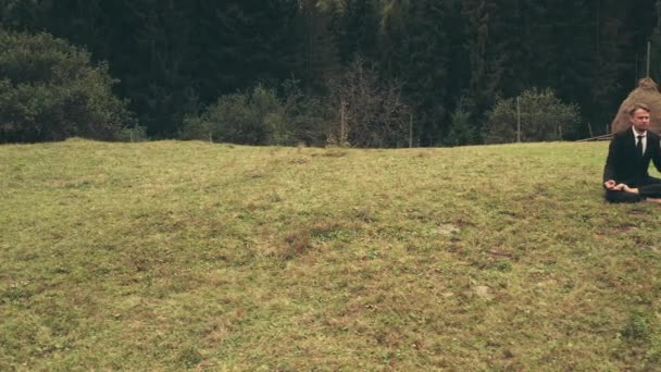 Zakenman in ontspannen houding zitten op gras antenne. Een dennenbos. Herfst natuur landschap — Stockvideo