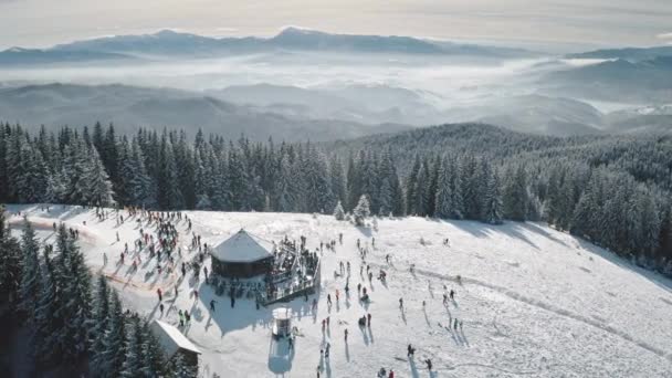 Centro deportivo de invierno en la cima de la montaña de nieve aérea. Gente en el paisaje natural. Pista de esquí en el bosque de abeto — Vídeo de stock