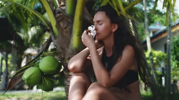 Thailanda stațiune closeup: femeia se odihnește în nuanța palmelor de nucă de cocos pe plaja de nisip cu flori tropicale — Videoclip de stoc