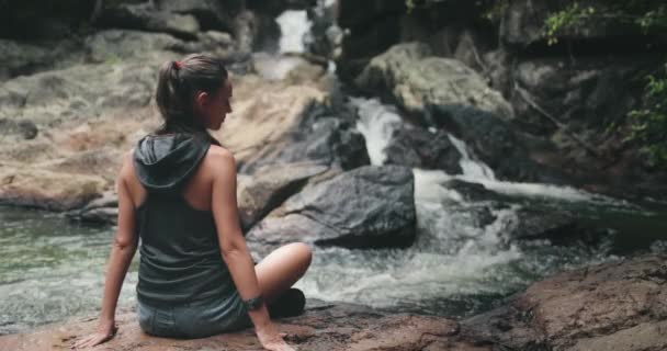 河流瀑布：女人躺在石头上。溪底的水流平静.女孩放轻松 — 图库视频影像