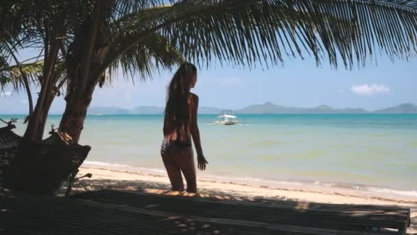 Slow motion ocean beach: kvinna koppla av på solstol i palm skugga. Söt flicka solbränna på solen, hängmatta — Stockvideo